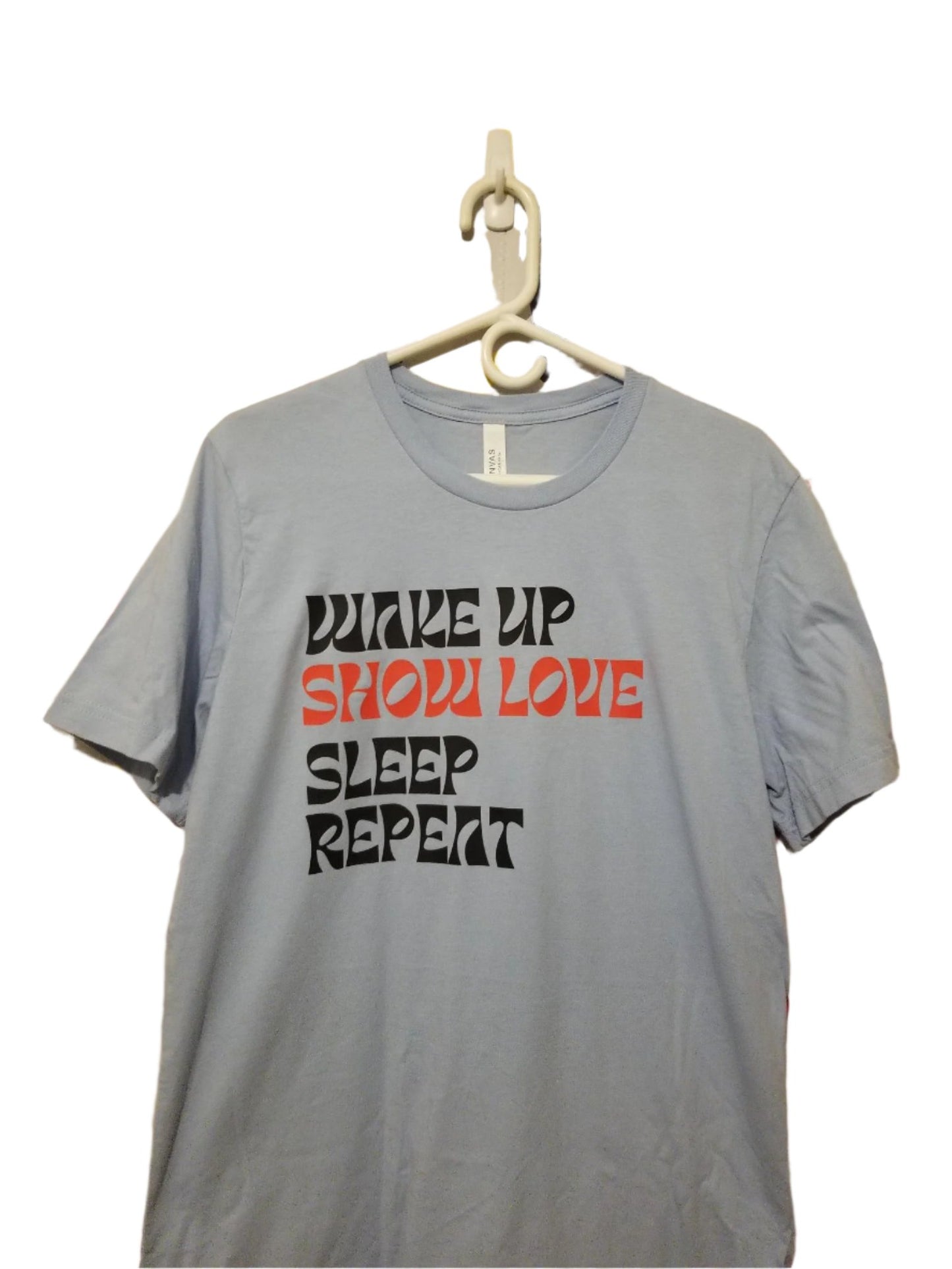 Baby Blue TShirt on a hanger with the words Wake Up Show Love Sleep Repeat. The words "Show Love" are in red while the others are in black.